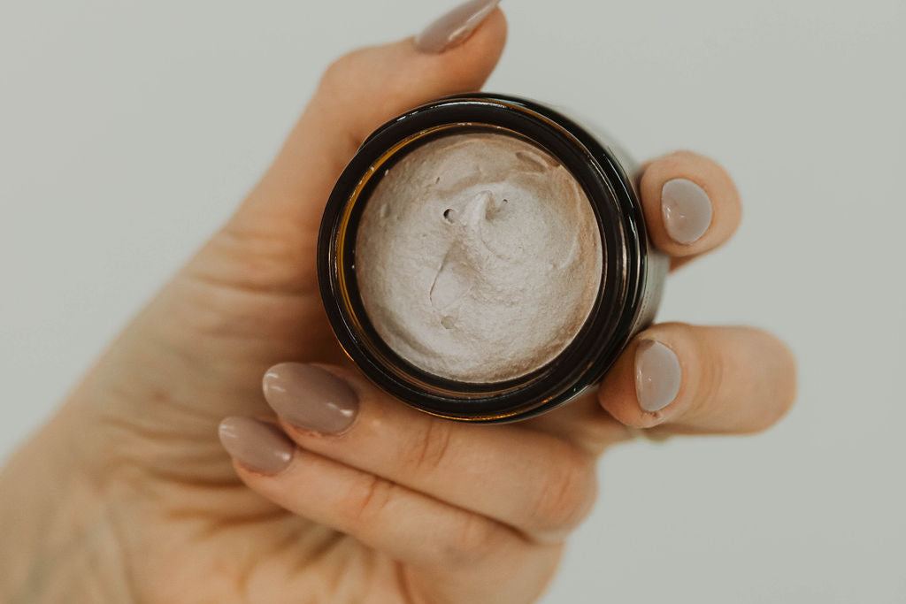 Hand holding a jar of tallow cream against a neutral background