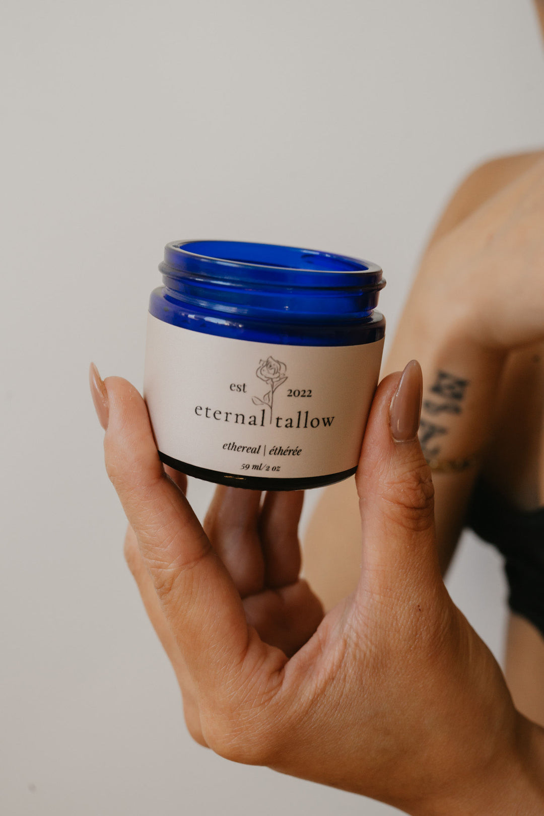 Hand holding a jar of 'eternal tallow' organic tallow lotion against a neutral background
