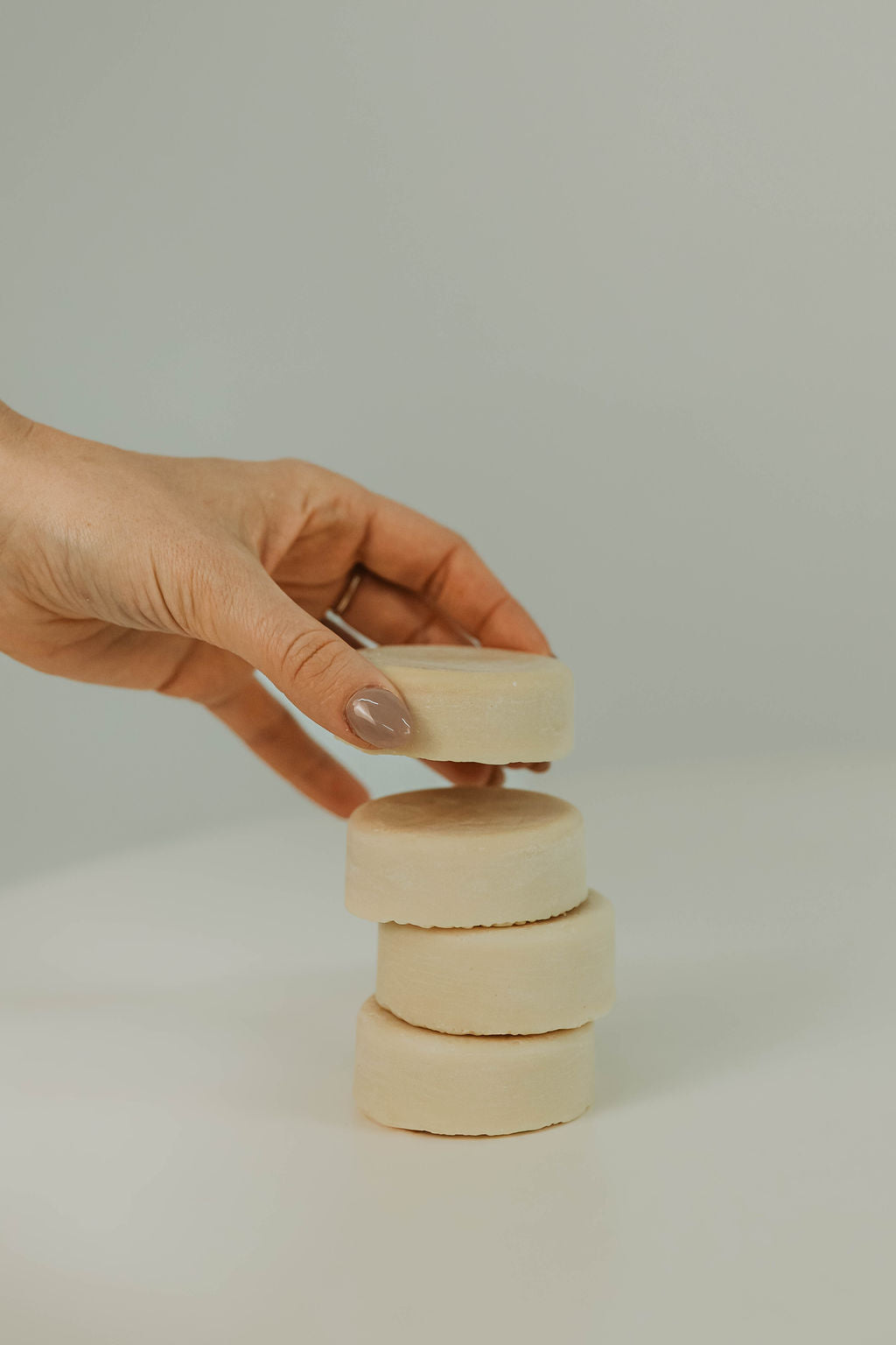 Hand stacking tallow hair conditioner discs on a plain background