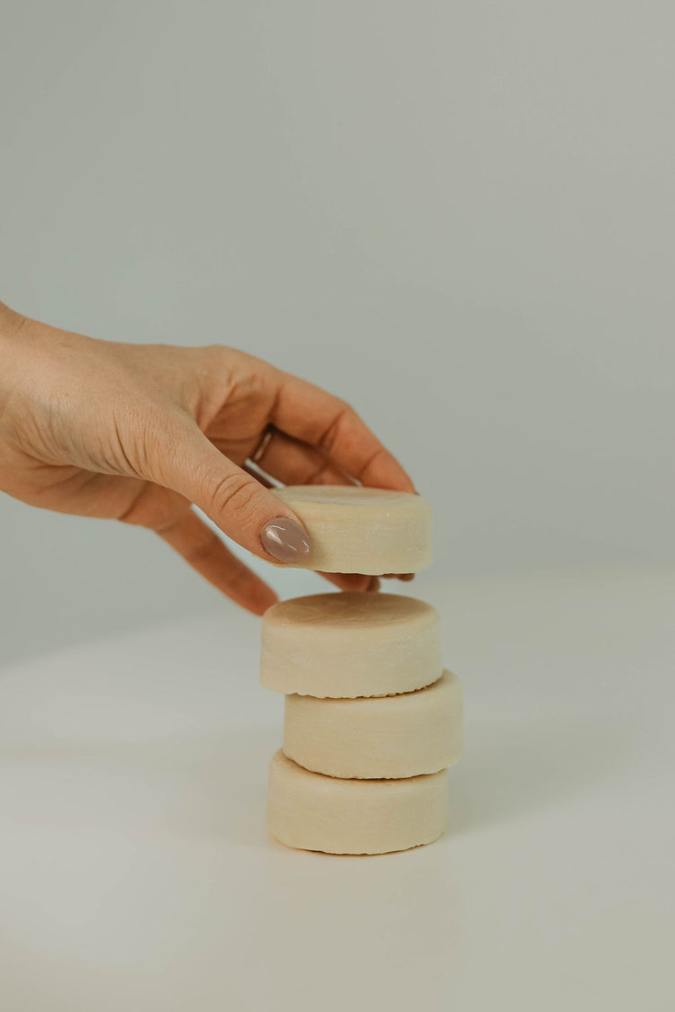 Hand stacking tallow hair conditioner discs on a plain background