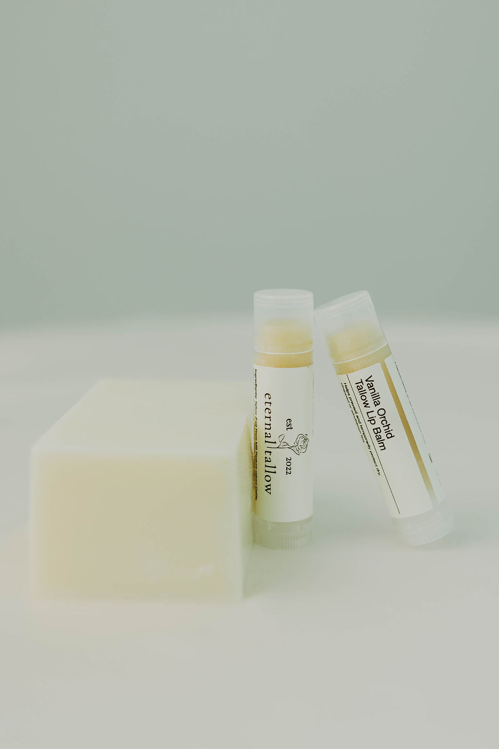 Bar of soap and two tubes of organic tallow lip balm on a white background