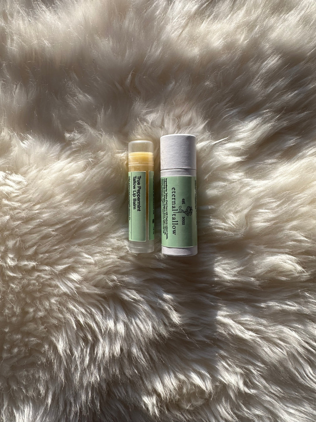Two containers of True Peppermint Tallow Lip Balm placed on a furry surface, with one container standing upright and the other lying down. 